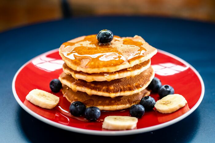 Stack of pancakes with syrup, blueberries, and banana slices on a red plate, illustrating smooth pickup lines concept.