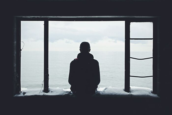 Silhouette of a person sitting by a window looking out at a gray sea, symbolizing job interview red flags toxic workplace.