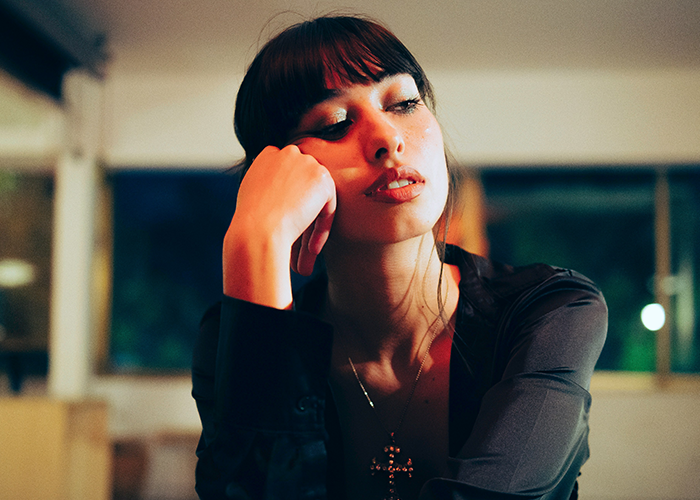 Young woman sitting indoors at night looking thoughtful, illustrating neighbor refuses tourists patio use and Airbnb discrimination.
