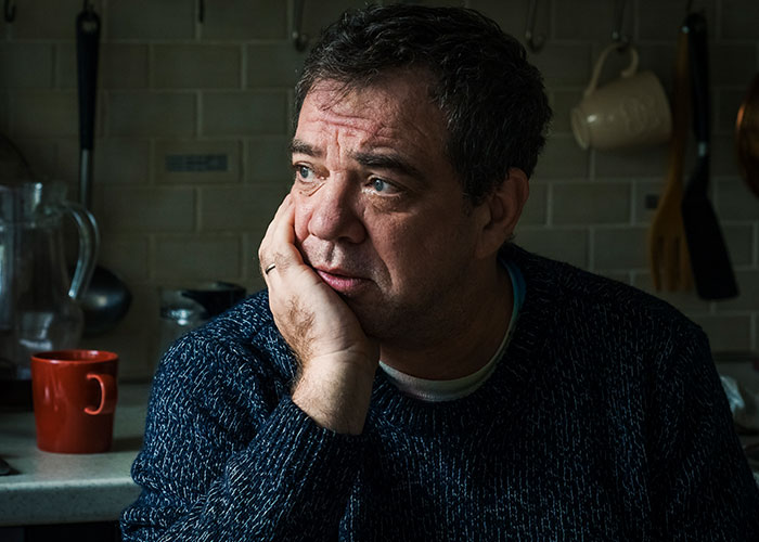Middle-aged man in a dark sweater looking thoughtful and distressed, reflecting on a strained father-daughter relationship.