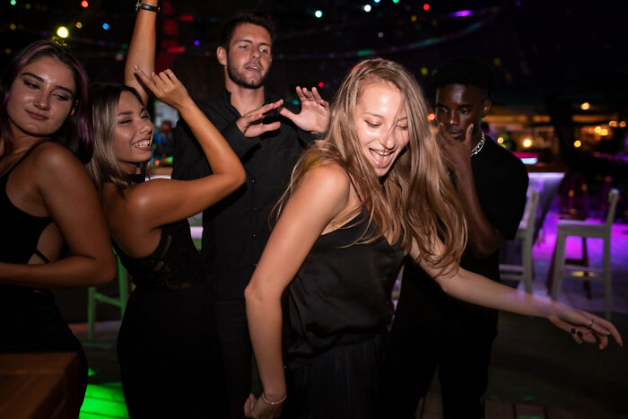 Group of young adults dancing at night, highlighting examples of everyday sexism and pressure women face socially.