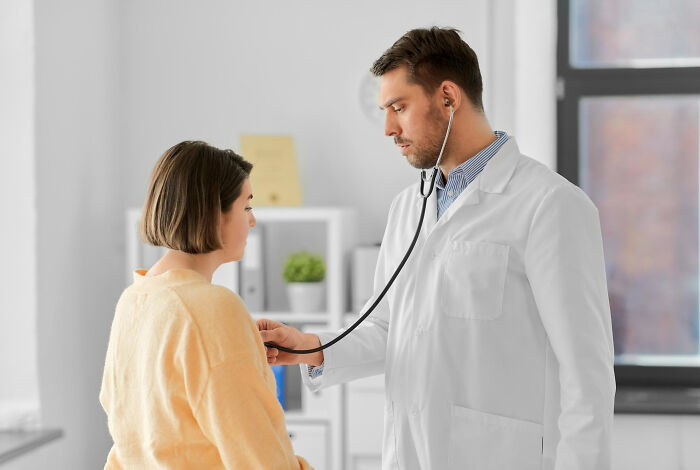 Doctor using stethoscope to examine woman, highlighting everyday sexism and pressure women face in healthcare settings.