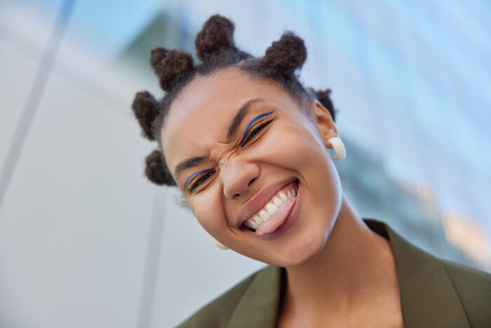 Smiling young woman with bantu knot hairstyle expressing confidence against a blurred urban background, highlighting everyday sexism.