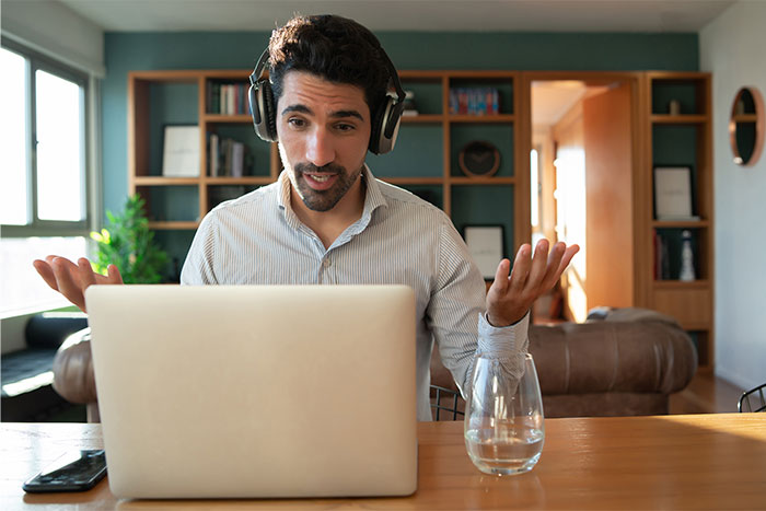 Man with headphones discussing surname refusal with American coworkers during a video call in a home office setting. - 1
