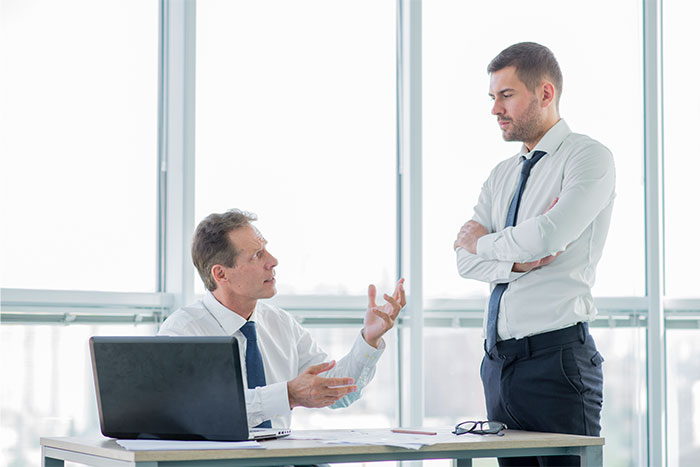 Two men in office setting having serious discussion, highlighting conflict over man refusing to change surname for coworkers. - 6
