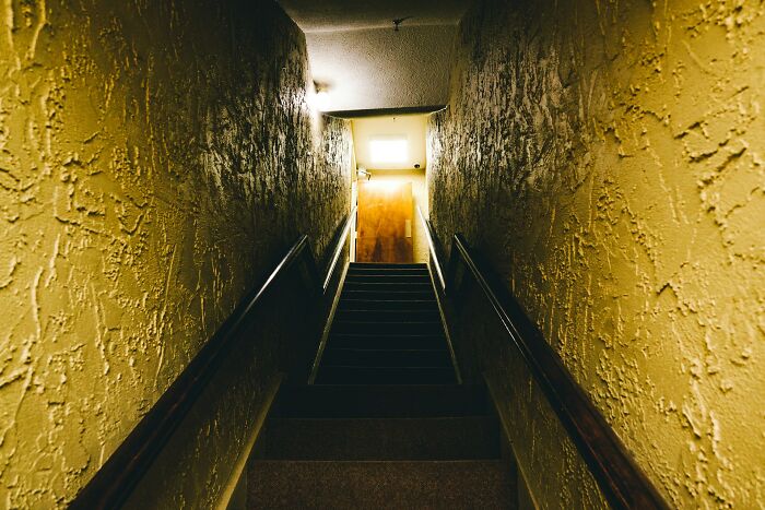 Dark narrow staircase with textured walls, dimly lit, evoking creepy and disturbing police home visit scenes.