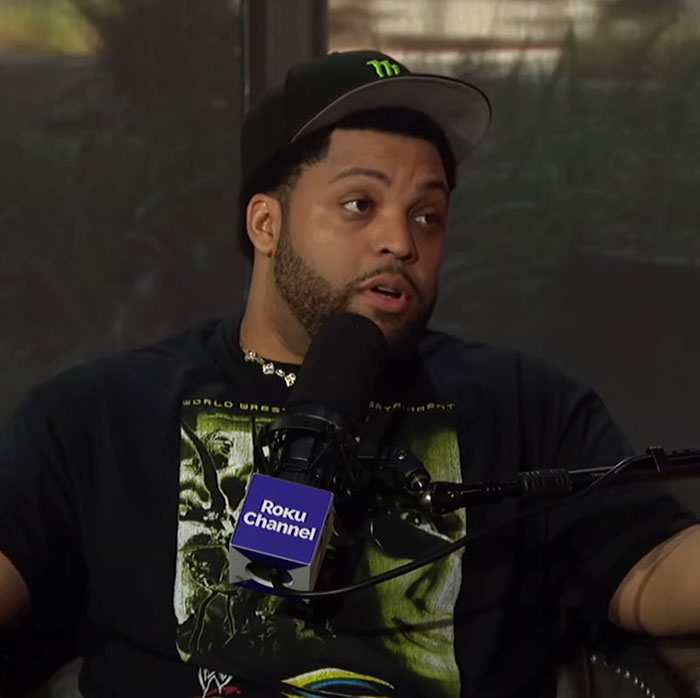 Man wearing black hat and graphic t-shirt speaking into a microphone with Roku Channel logo, discussing Ice Cube War Of The Worlds.