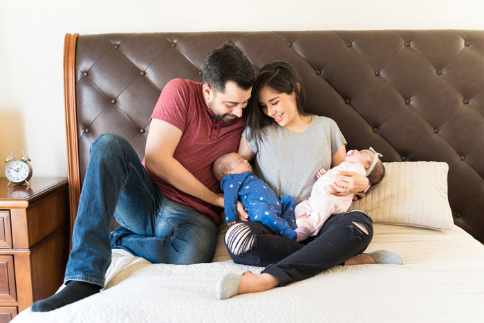 Young man defending his wife while holding twins, sitting together on a bed with a joyful family moment.