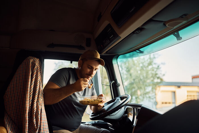 A man eating lunch inside a truck cabin, illustrating frustratingly out of touch bosses in a work environment.