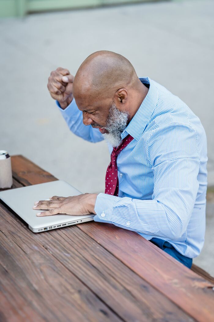 Frustrated man in a blue shirt and red tie angrily closing laptop, representing bosses being out of touch at work.