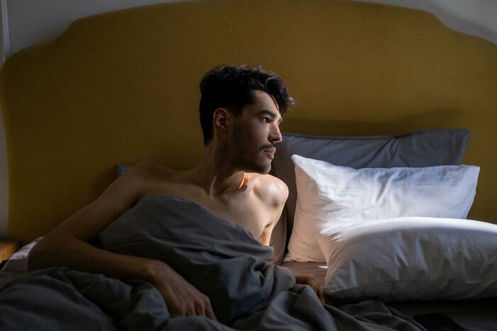 Man sitting in bed looking out a window, illustrating frustration and feeling out of touch with his surroundings.