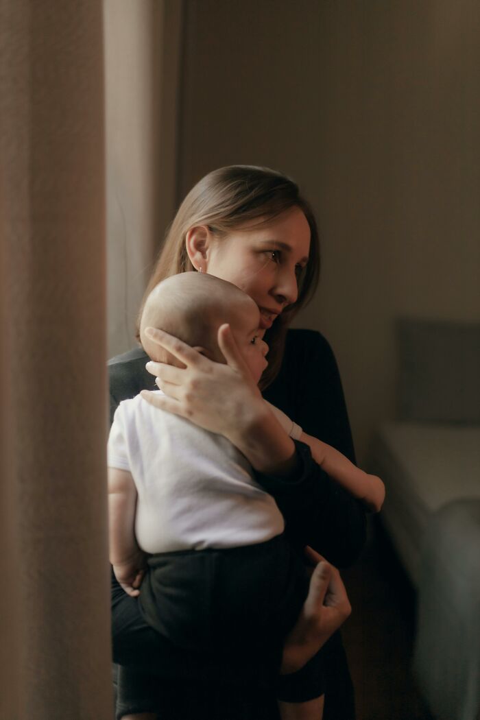 Woman holding baby by window, symbolizing challenging emotions related to bosses being frustratingly out of touch.