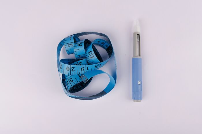 Blue measuring tape coiled next to a blue and white injection pen representing Ozempic side effects and lawsuits. Blue measuring tape coiled next to a blue and white injection pen representing Ozempic side effects and lawsuits.