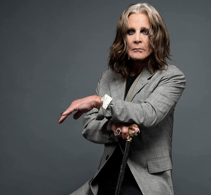 Ozzy Osbourne posing in a gray suit holding a cane, related to lawyers explaining buying a house with his grave.