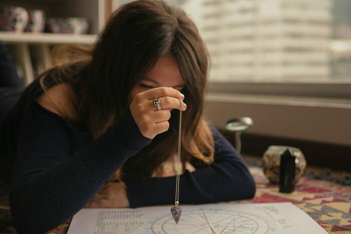 Woman using a pendulum over a chart, illustrating psychic predictions and people experiencing psychic insights.