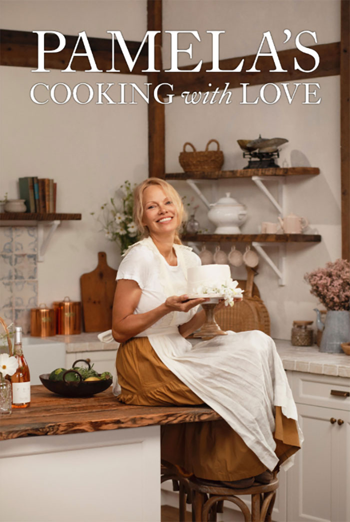 Pamela Anderson in kitchen holding a cake, promoting Pamela's cooking show with warm and rustic decor. - 8