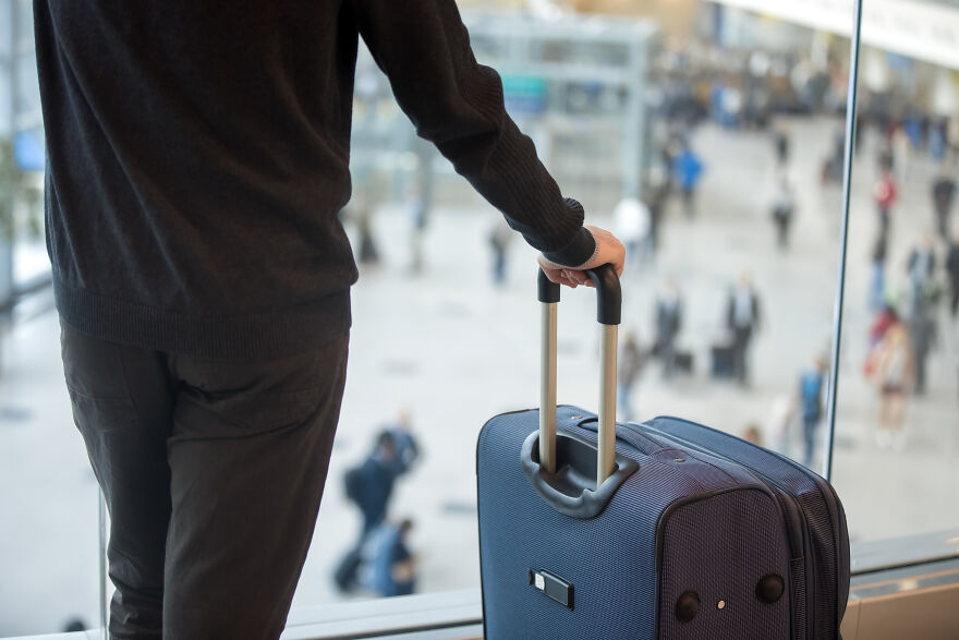 Person standing at airport window holding suitcase handle, capturing home alone vibes and travel abandonment scene.