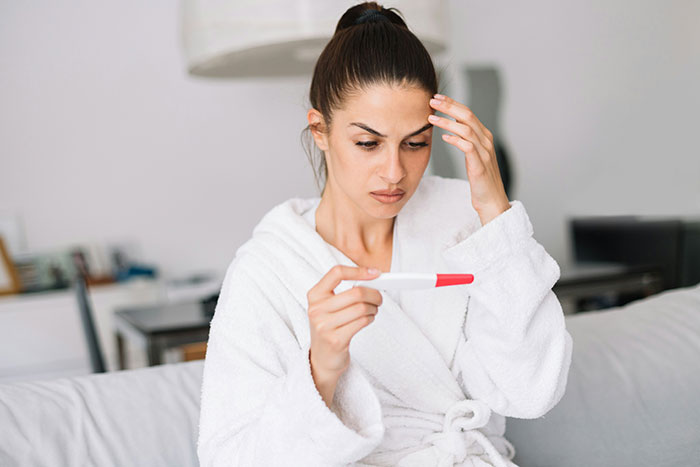 Woman in white robe looking worried while holding a pregnancy test, highlighting parents neglecting the child they had. - 22