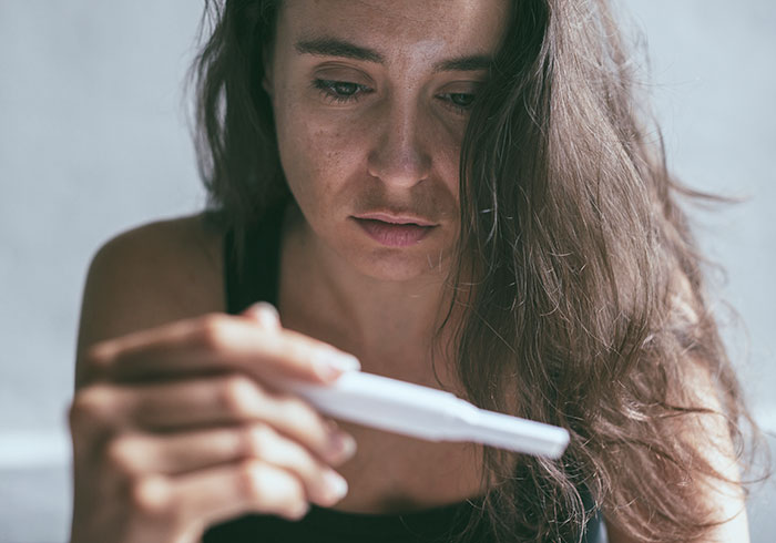 Woman looking sadly at a pregnancy test, reflecting on parents wanting kids but neglecting the one they had. - 11