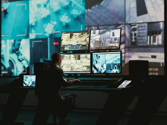 Night shift worker monitoring multiple security screens in a dark room, capturing chilling paranormal encounters on camera.