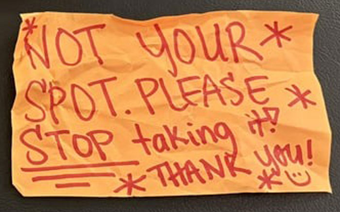 Handwritten anonymous note on orange paper attempting to trick woman into giving up her parking spot by dodgy neighbor.