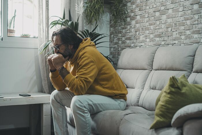 Man in a yellow hoodie sitting on a couch, deep in thought, illustrating what happened to the smartest kids in class.