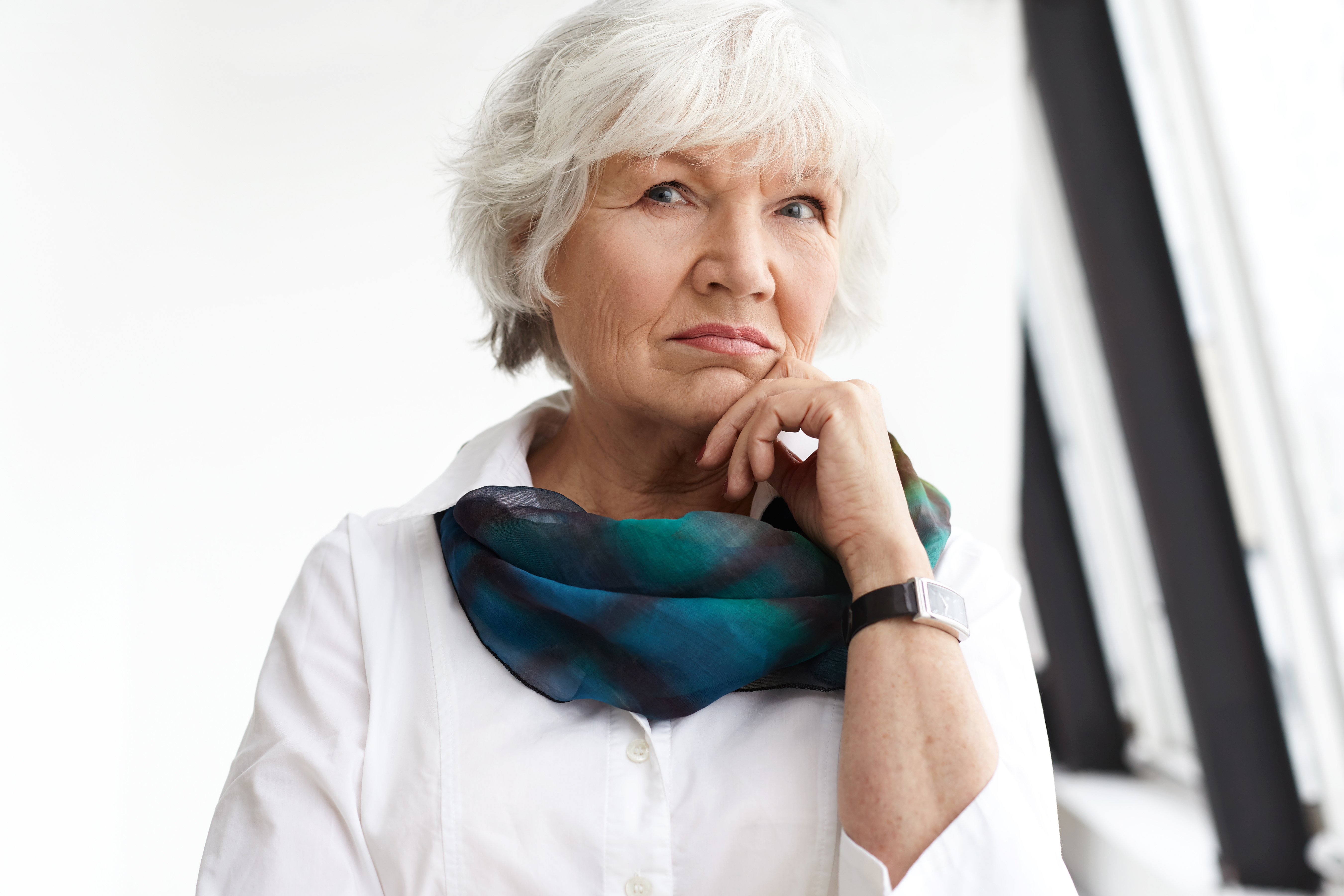 Thoughtful elderly woman with white hair in a white shirt and colorful scarf, symbolizing landlord&rsquo;s daughter and cool house claim.