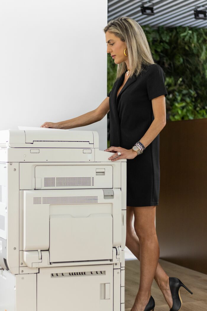Woman in black dress using office copier, illustrating coworker challenges and morons in workplace stories.