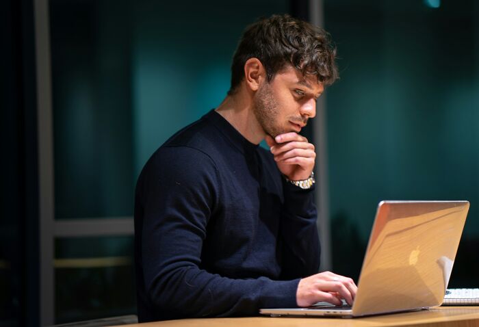 Young man working on a laptop, looking puzzled and deep in thought, illustrating coworker morons at work.