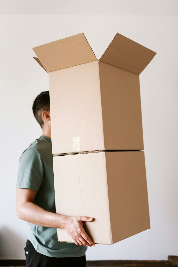 Person carrying two large cardboard boxes stacked, illustrating coworker morons struggling with simple tasks at work.