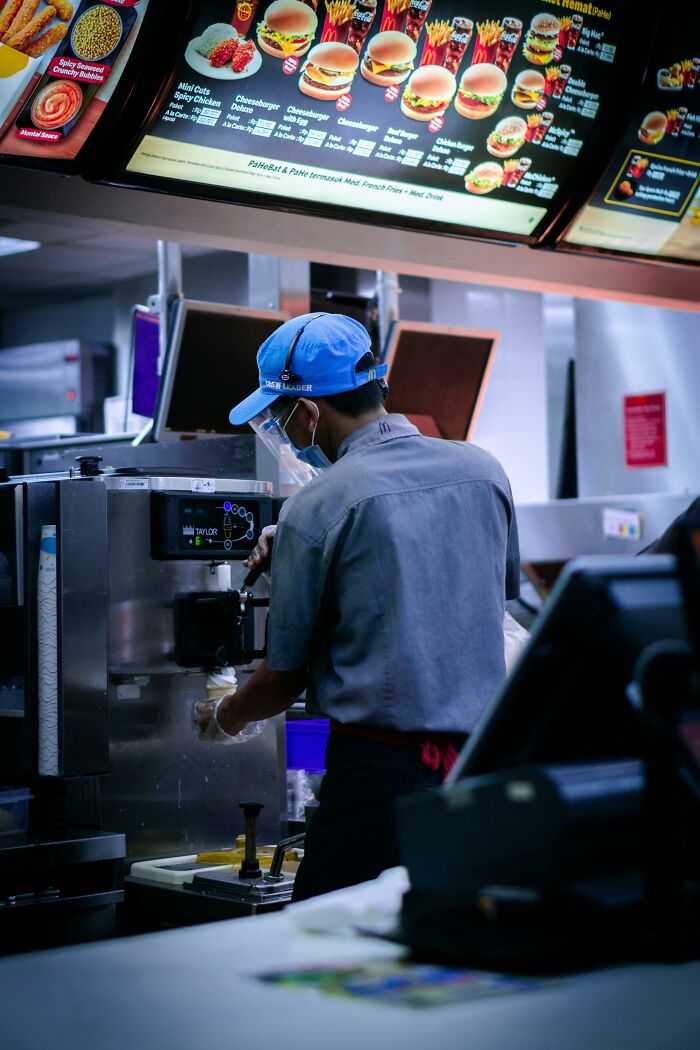 Fast food worker using soft serve machine behind counter in a restaurant, highlighting coworker work environment challenges.