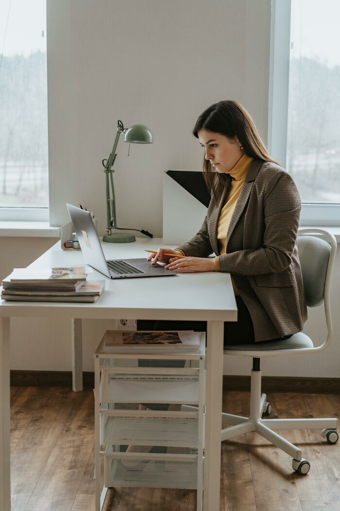 Woman working on laptop at desk in modern office, illustrating coworkers who are morons and workplace challenges.