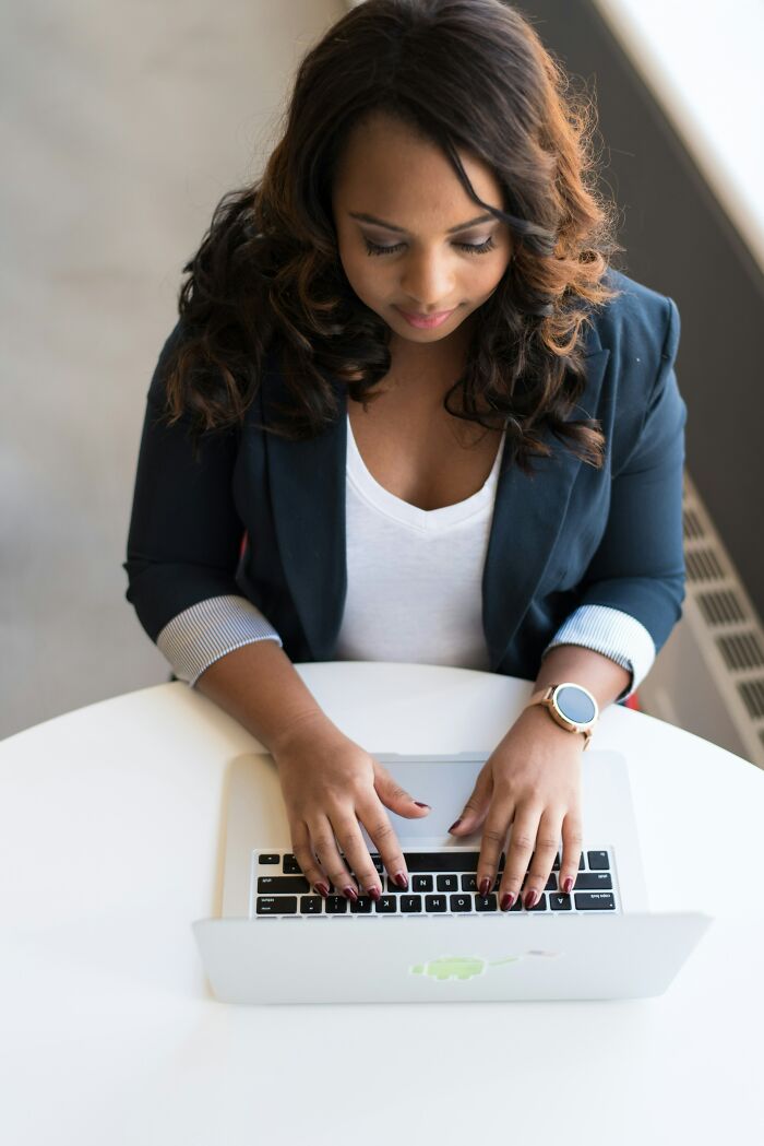 Woman coworker typing on a laptop at a round white table, illustrating stories of coworkers in an office setting.
