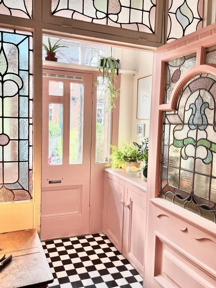 Pink vintage-style entryway with stained glass windows, checkerboard floor, and lush green plants as decor pieces.