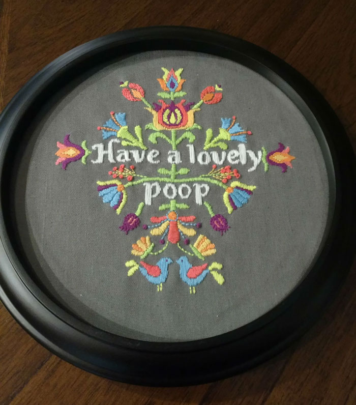 Embroidered decor piece with colorful floral and bird designs and humorous text in a black round frame for magical homes.