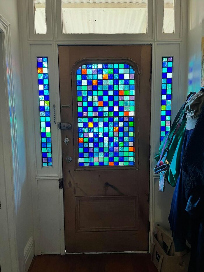 Stained glass decor pieces on front door and side panels creating a magical colorful light effect in the home entryway.