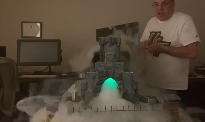 A man stands near a fog-emitting castle decor piece that adds a magical ambiance to a home setting.