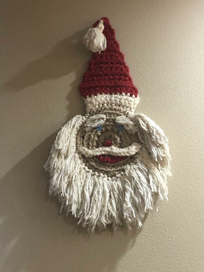 Crocheted Santa Claus wall decor piece hanging on beige wall adding a magical home decoration touch.