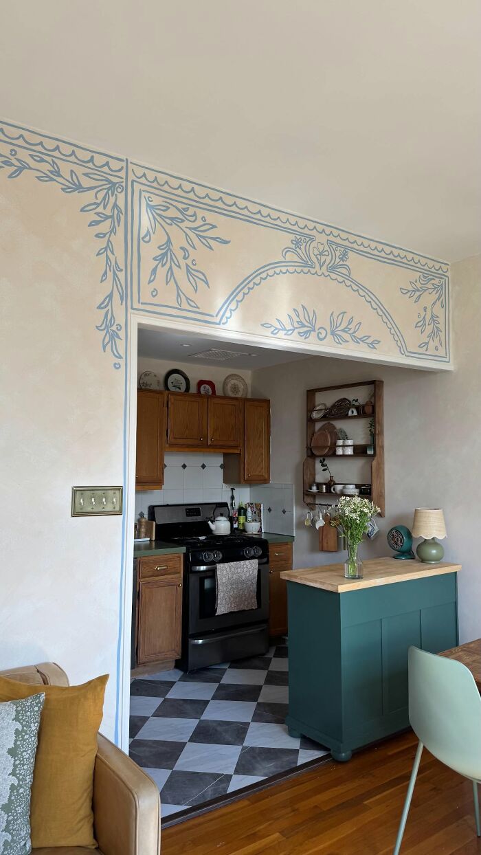 Cozy kitchen with magical decor pieces including painted wall designs, wooden cabinets, and a green kitchen island with flowers.