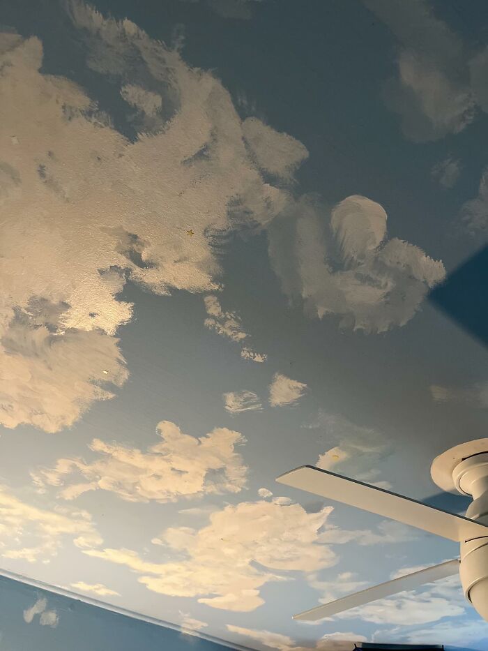 Ceiling decor piece painted with clouds creating a magical atmosphere in a home interior with a white ceiling fan.