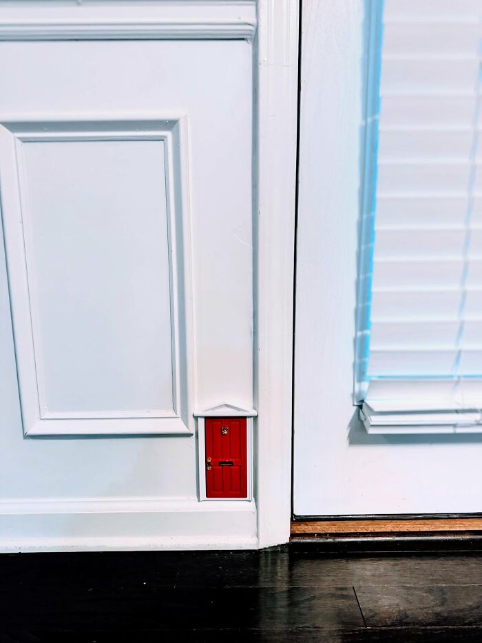 Small red decorative door installed on white interior wall near floor, adding magical decor piece to home ambiance.