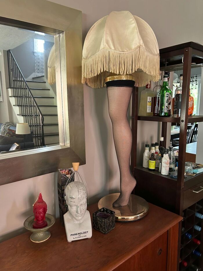 Leg lamp decor piece with fringe shade, phrenology head sculpture, and eclectic home decor on wooden sideboard.