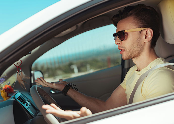 Young man in sunglasses sitting in car, expressing confusion or frustration while experiencing a personal mystery.