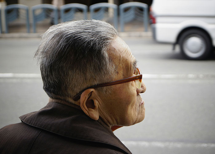 Elderly man with glasses looking thoughtfully across a street, evoking mysteries people personally experienced.