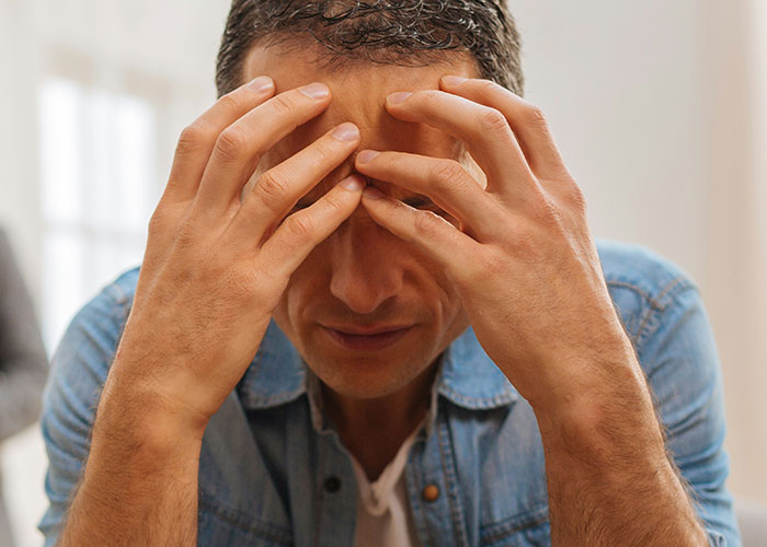 Man in denim jacket holding head in hands, appearing stressed or confused, reflecting unexplained mysteries experienced.
