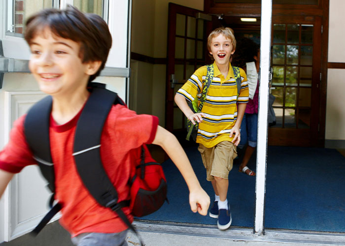 Two young boys with backpacks happily running out of a school building, capturing a moment of mystery and surprise.