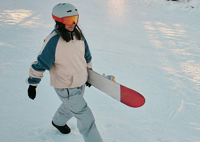 Woman in winter sports gear carrying a snowboard on snow, illustrating mysteries people personally experienced outdoors.