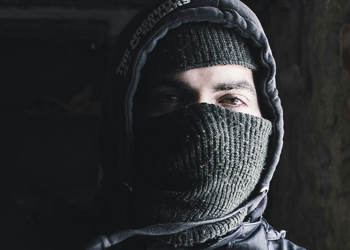 Person wearing dark hood and knitted face covering, symbolizing mysterious and unexplained personal experiences and mysteries.