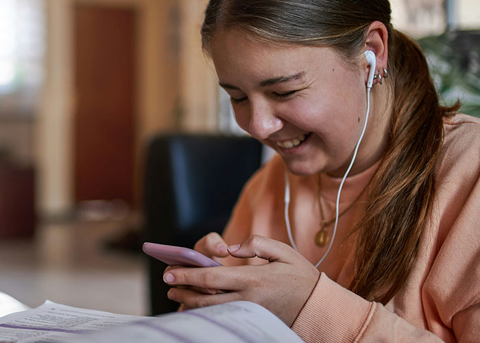 Young woman smiling while using smartphone with earphones, reflecting personal mysteries people experienced and can't explain.