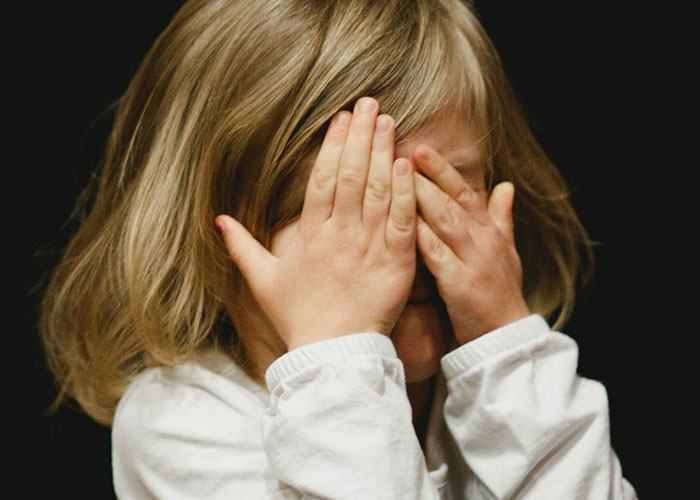 Young child covering face with hands, illustrating mysteries people personally experienced and still can’t explain.